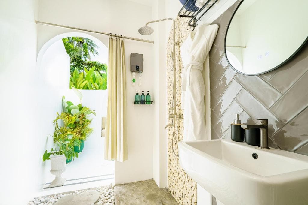 Open-air bathroom with rain shower, stone wall, and tropical garden view